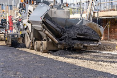 Sıcak asfalt kaldırım taşı yeni yerleşim alanı üzerine yeni yol yüzeyi döşeyen ve yanında turuncu hi-viz 'deki yol işçisi operatörü