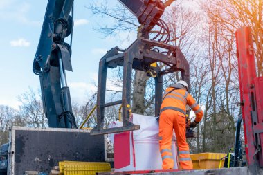Dropside plakalı HIAB vinç kamyonu tuğla kapma eklentisiyle inşaat alanına malzeme getiriyor ve indiriyor.