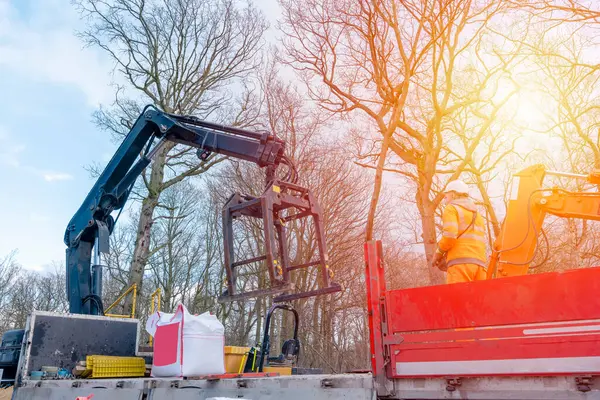 Dropside plakalı HIAB vinç kamyonu tuğla kapma eklentisiyle inşaat alanına malzeme getiriyor ve indiriyor.