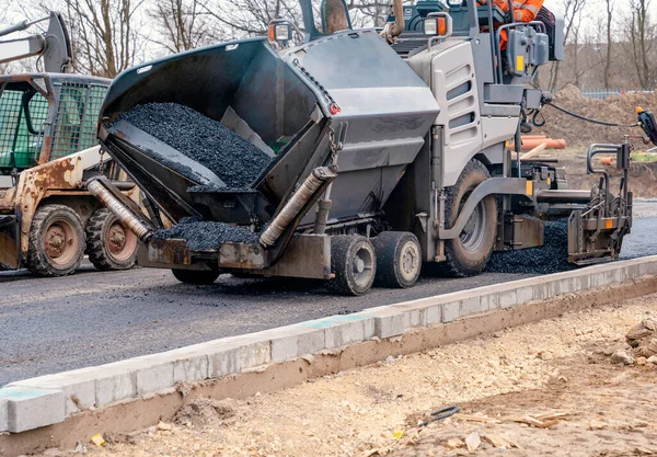Sıcak asfalt kaldırım taşı yeni yerleşim alanı üzerine yeni yol yüzeyi döşeyen ve yanında turuncu hi-viz 'deki yol işçisi operatörü