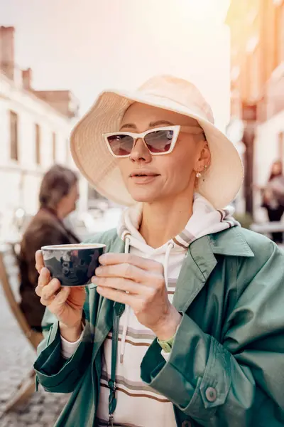 an extravagant happy woman in green coat and white hat having breakfast coffee in a cafe