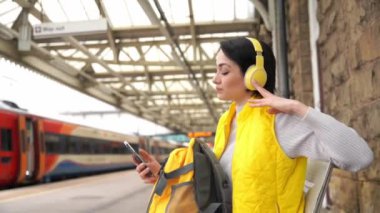 Tren istasyonunda kulaklıkla müzik dinleyen genç bir kadın müzik eşliğinde seyahat kavramının tadını çıkarıyor.