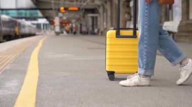 Platformdaki tren istasyonunda sarı bavullu bir yolcu bekliyor. Seyahat kavramı.
