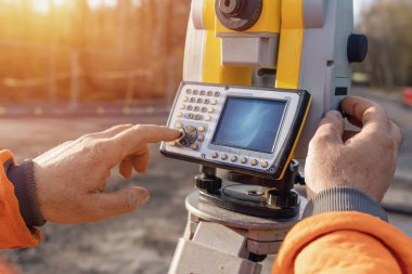 Site engineer operating his instrument during roadworks. Builder using total positioning station tachymeter on construction site for new road setting out clipart