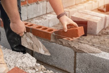İnşaat alanındaki çimento karışımına tuğla döşeyen duvarcı. Daha ekonomik konut kavramları inşa ederek konut krizini azaltmak