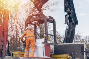 Dropside plakalı HIAB vinç kamyonu tuğla kapma eklentisiyle inşaat alanına malzeme getiriyor ve indiriyor.