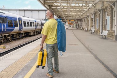 Elinde bavul ve takım elbisesi olan gezgin tren istasyonunda tren bekliyor. Seyahat kavramı.