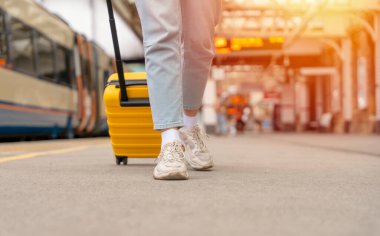 Platformdaki tren istasyonunda sarı bavullu bir yolcu bekliyor. Seyahat kavramı.