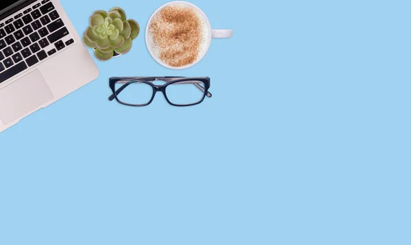 Top view workspace on blue background with laptop, plant, coffee, glasses. Space for text. The financial checks