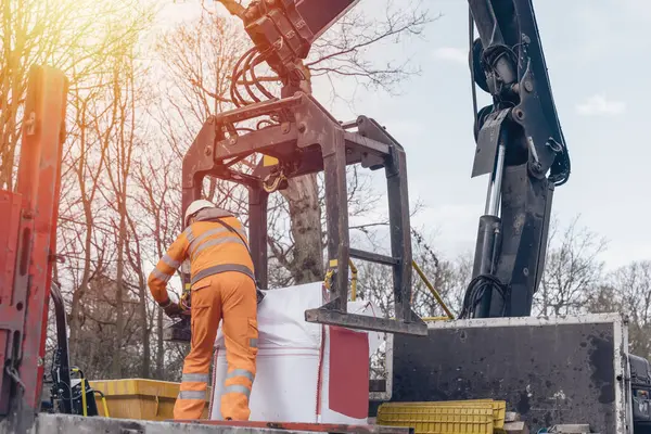 Dropside plakalı HIAB vinç kamyonu tuğla kapma eklentisiyle inşaat alanına malzeme getiriyor ve indiriyor.