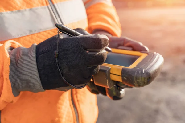 Site engineer operating his touch screen controller instrument during roadworks. Builder using touch screen controller to control total positioning station tachymeter on construction site for new road setting out