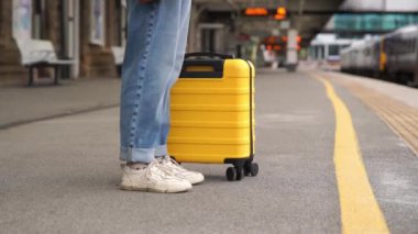 Platformdaki tren istasyonunda sarı bavullu bir yolcu bekliyor. Seyahat kavramı.