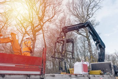 Dropside plakalı HIAB vinç kamyonu tuğla kapma eklentisiyle inşaat alanına malzeme getiriyor ve indiriyor.