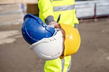 Yüksek çözünürlüklü yansıtıcı takım giyen bir müteahhit kask seçimi yapar. İnşaat personeli, mühendis ve inşaat işçileri için her zaman güvenlik ve kişisel koruyucu ekipman kullanın. İnşaat alanı kavramında her zaman doğru PPE kullan