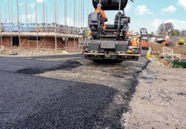 Sıcak asfalt kaldırım taşı yeni yerleşim alanı üzerine yeni yol yüzeyi döşeyen ve yanında turuncu hi-viz 'deki yol işçisi operatörü