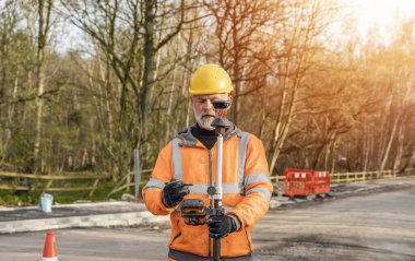 Yol çalışması sırasında dokunmatik ekran kontrol cihazını çalıştıran site mühendisi. İnşaatçı, yeni yol ayarları için inşaat alanındaki toplam konumlandırma istasyonu taksimetresini kontrol etmek için dokunmatik ekran denetleyici kullanıyor