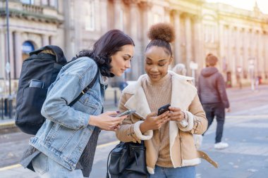 Kot ceketli iki kadın birbirleriyle konuşuyor, gülüyorlar, telefon izliyorlar ve tren istasyonunda hayat tarzı konseptini bekliyorlar.