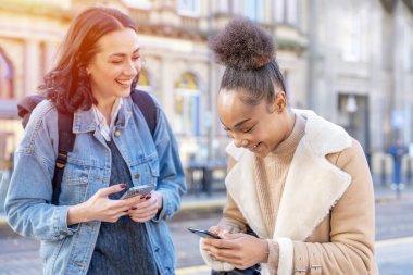 Kot ceketli iki kadın birbirleriyle konuşuyor, gülüyorlar, telefon izliyorlar ve tren istasyonunda hayat tarzı konseptini bekliyorlar.