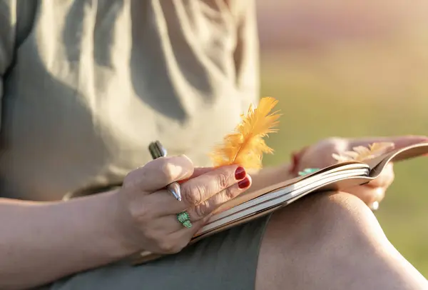 A woman holds a pen, a diary and a pen in nature. The concept of a lifestyle in travel. The concept of local tourism.