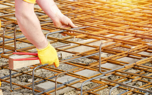 Steel fixer assembling reinforcement cage off rebars. Selective focus