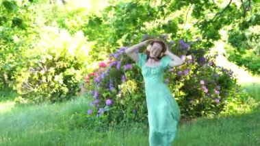 Açık havada, yeşil elbiseli ve kulaklıklı, halka açık parkta dans eden mutlu kızıl saçlı kadının portresi. Çevrimiçi müzik dinleyip kendin ol.