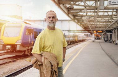 Elinde bavul ve takım elbisesi olan gezgin tren istasyonunda tren bekliyor. Seyahat kavramı.
