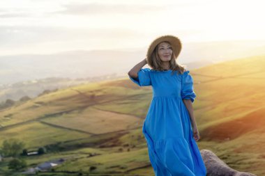Mavi elbiseli Asyalı kadın ve elinde lavanta buketi olan bir şapka yaz günbatımında dağın tepesinde.