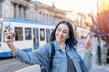 Tramvay durağında cep telefonu kullanan kot ceketli mutlu kadının açık hava portresi.