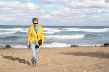 Güneşli bir günde deniz kenarında yürüyen mavi ceketli bir kadın bir turist kasabasına geldi. Seyahat yaşam tarzı konsepti