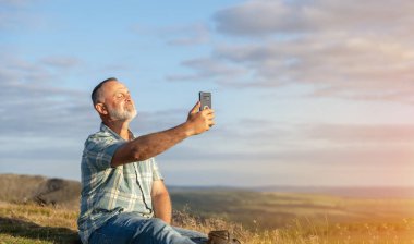 Mavi gömlekli sakallı bir gezgin dağlarda geziyor ve Peak District 'te telefonla fotoğraf çekiyor. Yerel turizm yaşam tarzı konsepti.