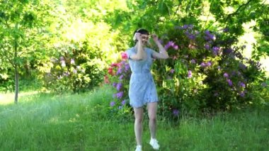 Açık havada, yeşil elbiseli ve kulaklıklı, halka açık parkta dans eden mutlu kızıl saçlı kadının portresi. Çevrimiçi müzik dinleyip kendin ol.