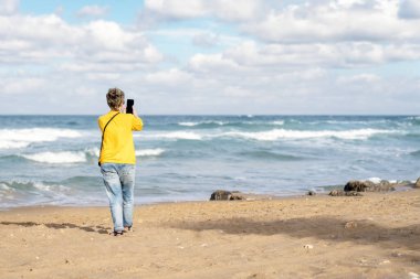 Güneşli bir günde deniz kenarında yürüyen sarı ceketli bir kadın bir turist kasabasına geldi. Seyahat yaşam tarzı konsepti