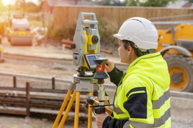 Bir inşaat şantiyesinde Theodolite toplam EDM ekipmanıyla çalışan bir kadın inşaat mühendisinin yakın plan portresi.