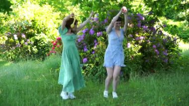Halka açık parkta dans eden iki mutlu kadının, kız arkadaşların, elbiseli ve kulaklıklı arkadaşlarının açık hava portresi. Çevrimiçi müzik dinleyip kendin ol.