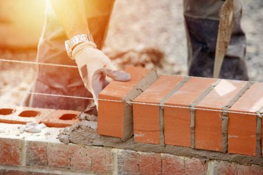 Industrial bricklayer laying bricks on cement mix on construction site close-up