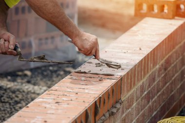 Close up of a brick wall and jointer trowel used by the worker to apply and level the mortar between bricks. Bricklayer making finishing touches to the brick wall and filling joints with mortar