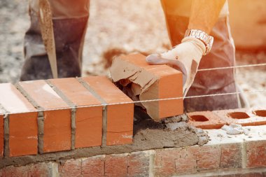 Industrial bricklayer laying bricks on cement mix on construction site close-up