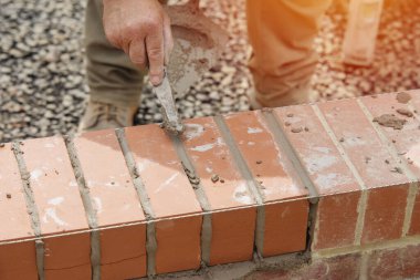 Close up of a brick wall and jointer trowel used by the worker to apply and level the mortar between bricks. Bricklayer making finishing touches to the brick wall and filling joints with mortar