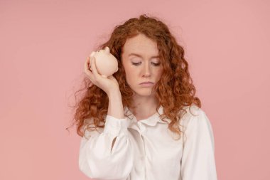 Beyaz gömlekli üzgün kadın, kumbarasını boş buluyor. Yatırım, tasarruf, para, depozito. Pembe arka planda kapalı stüdyo çekimleri.