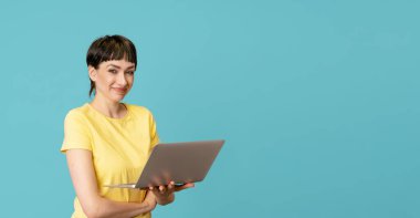 Sarı tişörtlü gülümseyen kadın dizüstü bilgisayar kullanıyor mavi arka planda kopya alanı olan bilgisayar. Çalışmak, sanal eğitim, e-öğrenme, online eğitim webinar konsepti izlemek
