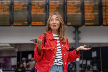 Kafası karışmış, sırt çantalı, akıllı telefonlu bir Asyalı kadın tren istasyonunda ve tren geliyor. Seyahat konseptinin tadını çıkarıyor.