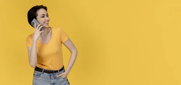 happy woman in yellow t-shirt and jeans   using a mobile phone on yellow background Copy space