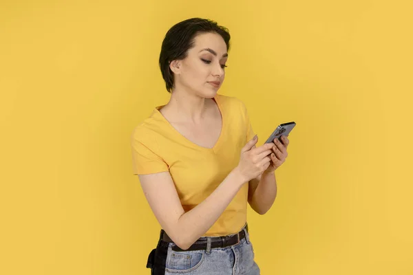surprised woman in yellow t-shirt and jeans   using a mobile phone on yellow background