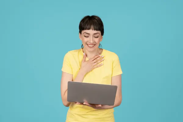 happy woman in a yellow t-shirt using laptop, pc computer on blue background.  Work studying, virtual training, e-learning, watching online education webinar concept