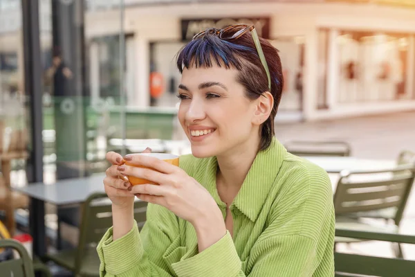 smiling woman  in green jacket having coffee at the street cafe outside, having fun time. lifestyle concept