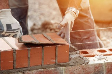 Industrial bricklayer laying bricks on cement mix on construction site close-up