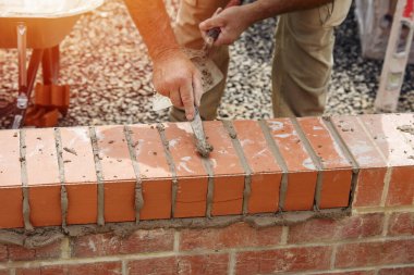 Close up of a brick wall and jointer trowel used by the worker to apply and level the mortar between bricks. Bricklayer making finishing touches to the brick wall and filling joints with mortar