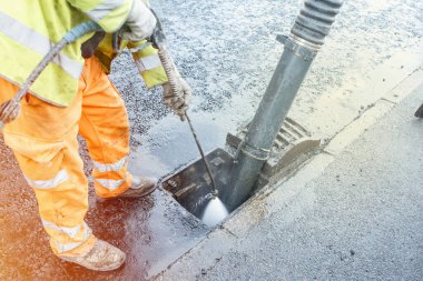 Builder cleaning blocked road gully with shovel and vacuum excavator clipart