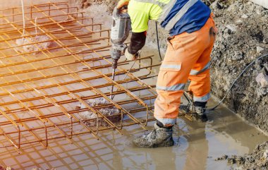 İnşaatçı üzerine takviye kafesi sığdırmak için tepesinden beton kıran elektrikli fren farı kullanıyor.