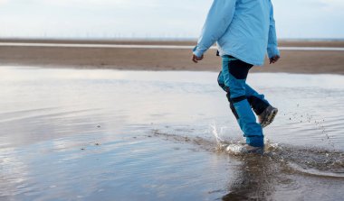 Sahilde koşan mavi pantolonlu ve botlu kadın. Seyahat yaşam tarzı konsepti